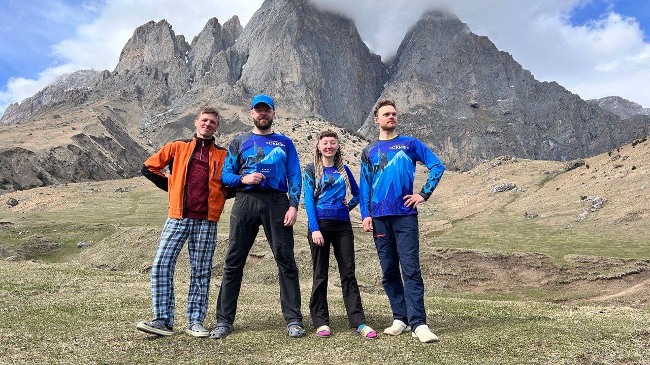 Четверо участников клуба в футболках «СКИФ» на фоне скальных башен